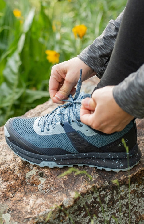 Woman tying KURU Footwear ATOM Trail Women's Sneaker in JetBlack-DarkTeal while hiking. perfect for heel pain. Providing Heel Pain Relief
